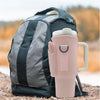 A pink adjustable water bottle carrier bag with a built-in phone pocket resting on a rocky surface.