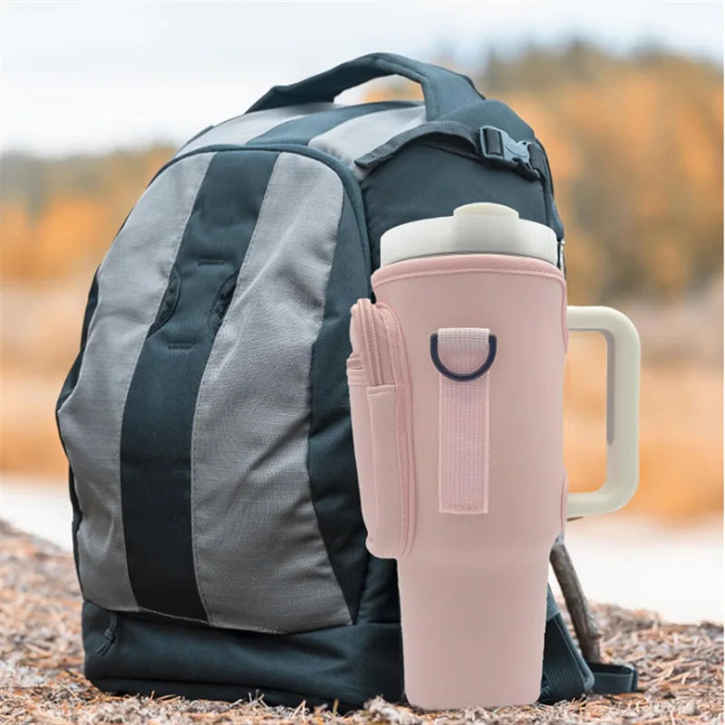 A pink adjustable water bottle carrier bag with a built-in phone pocket resting on a rocky surface.