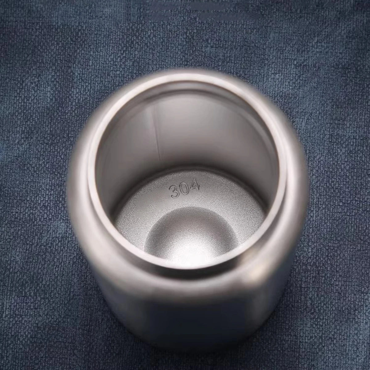 A silver stainless steel sport water bottle sitting on a dark blue fabric surface.
