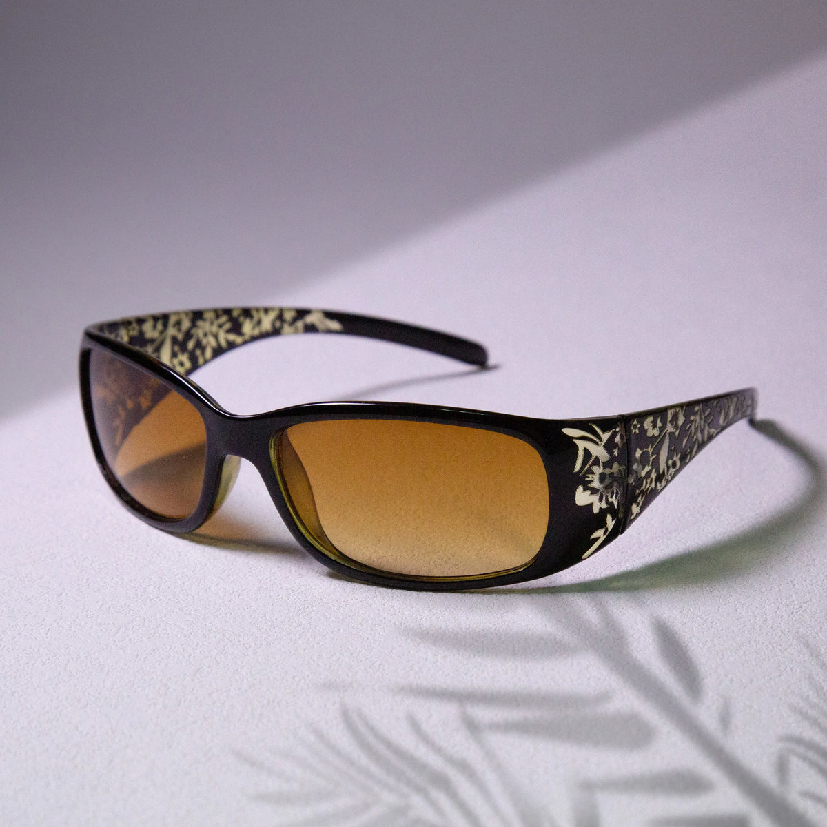 Un par de gafas de sol con montura cuadrada, patrón Y2K blanco y negro en las patillas y lentes ámbar.