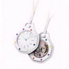 A white octagonal pocket watch pendant with a clear face and decorative elements, suspended by white strings.