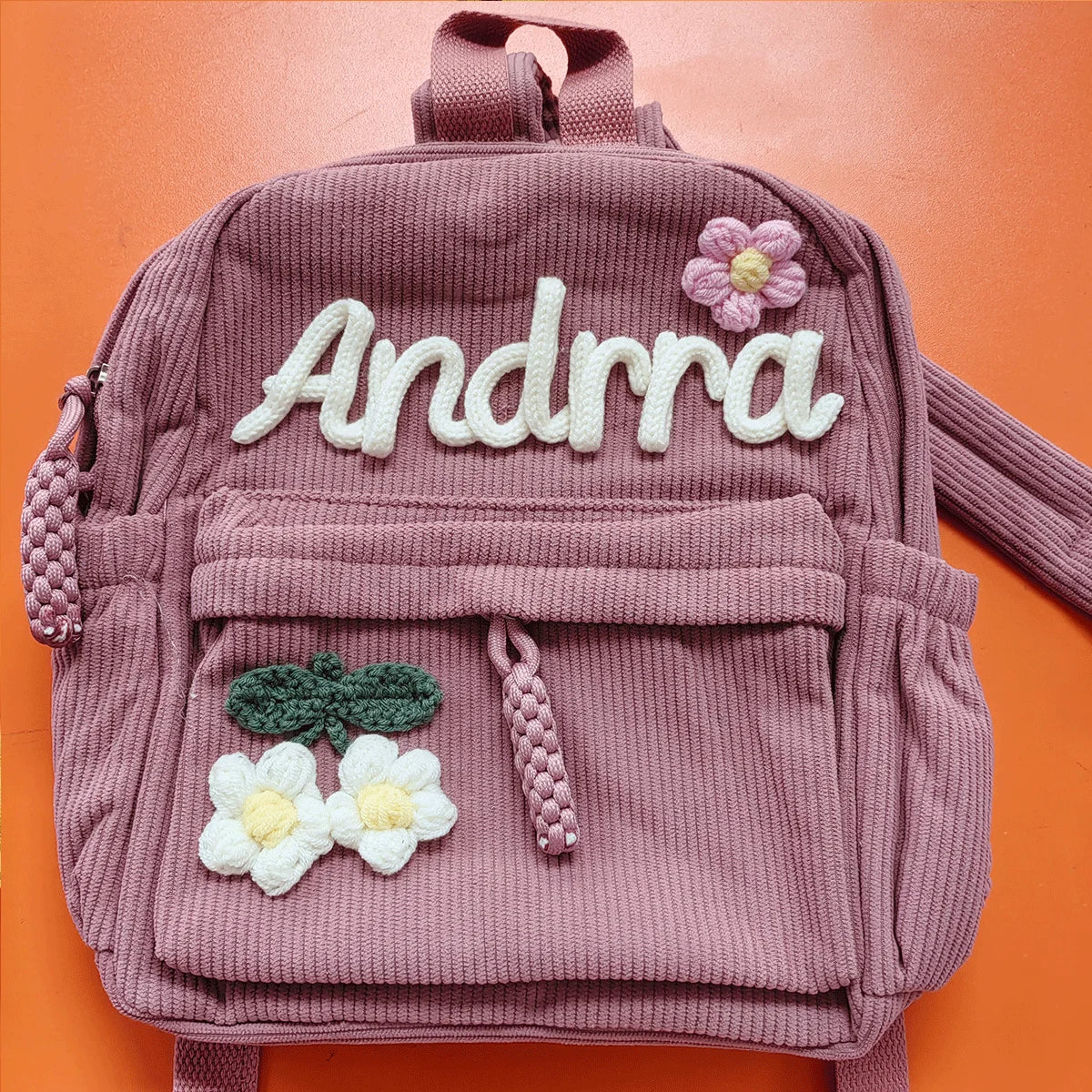 Rosa Samt-Rucksack mit der eingestickten Aufschrift Andrra und Blumenapplikationen