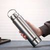 A hand holds a silver stainless steel sports water bottle with a hinged lid against a light background.