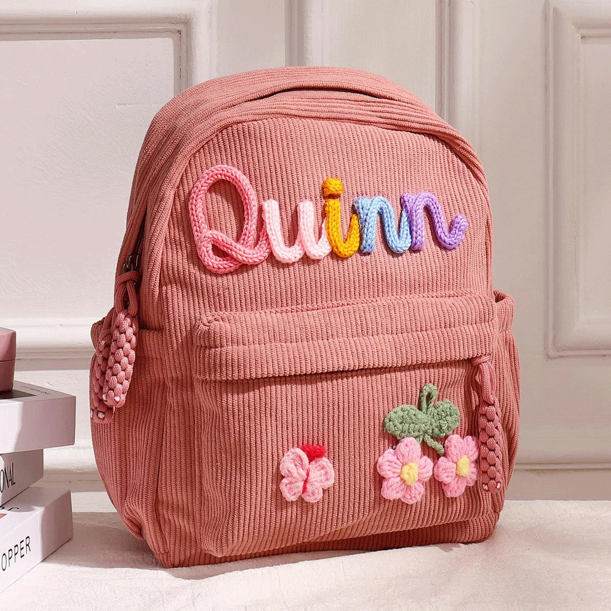 Rosa Corduroy Rucksack mit dem Namen Quinn in farbiger Fadenstickerei.