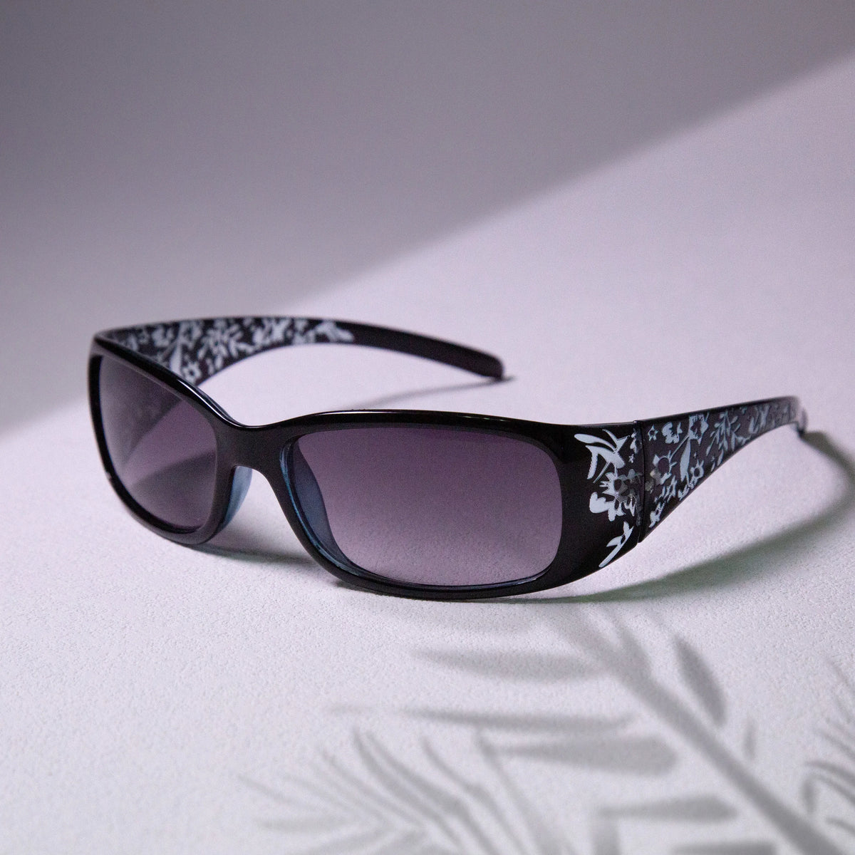 Gafas negras con estampado Y2K blanco en marco cuadrado sobre una superficie clara.
