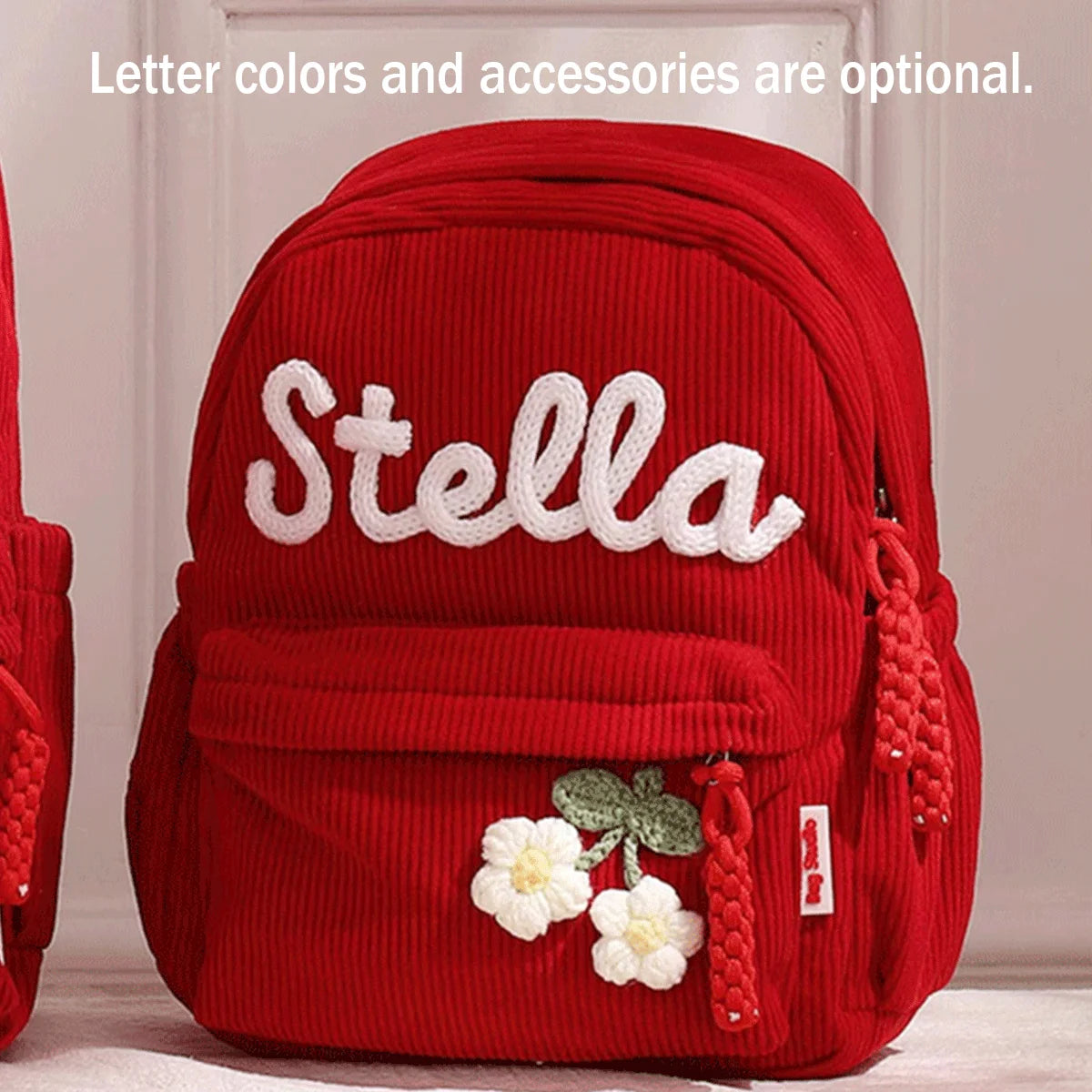 Helles rotes Cordhosen-Rucksack mit dem Namen Stella und weißen Blumenaccessoires.