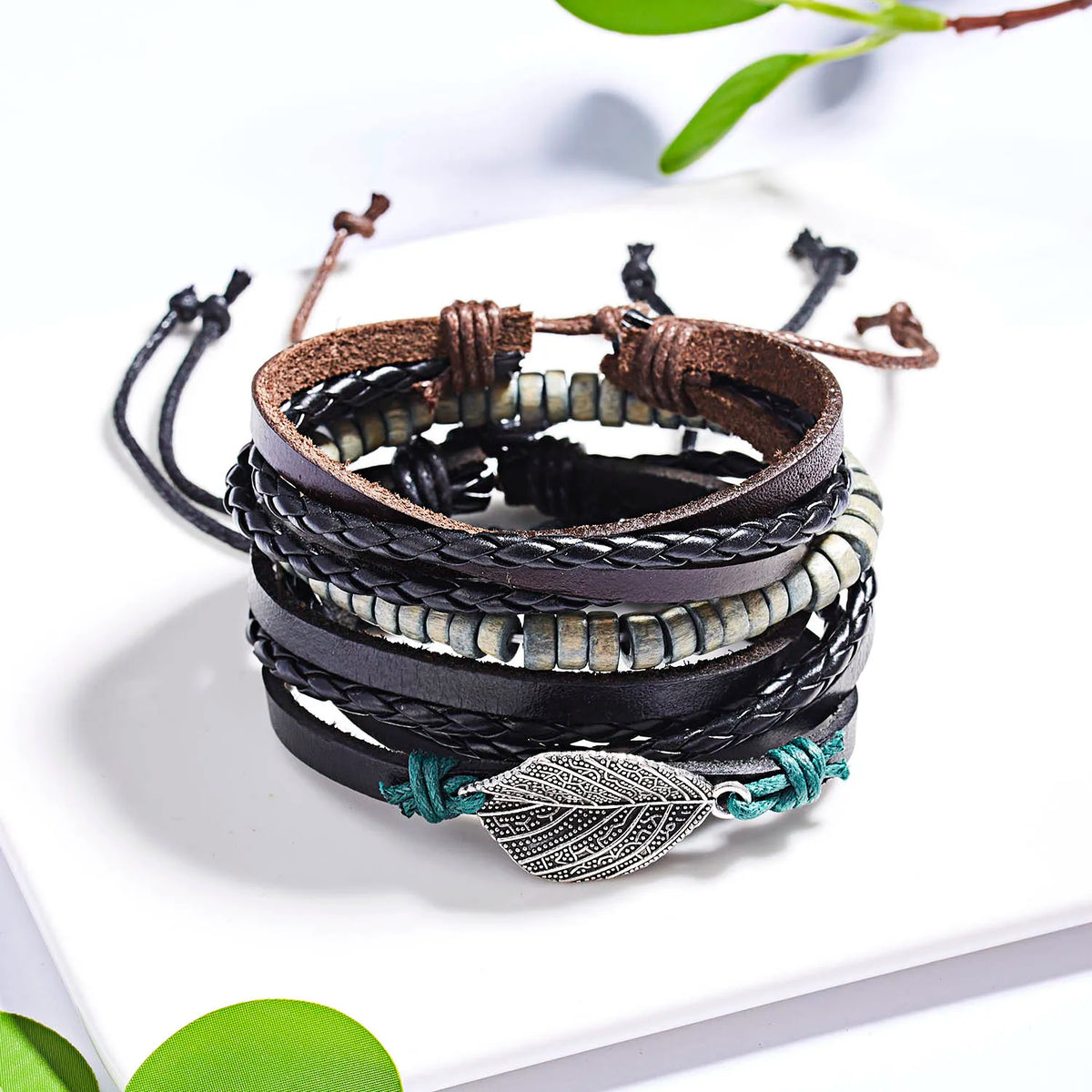 Stapel handgefertigter Lederarmbänder mit dunklen braunen und schwarzen Lederbändern und Blätter-Feder-Anhängern