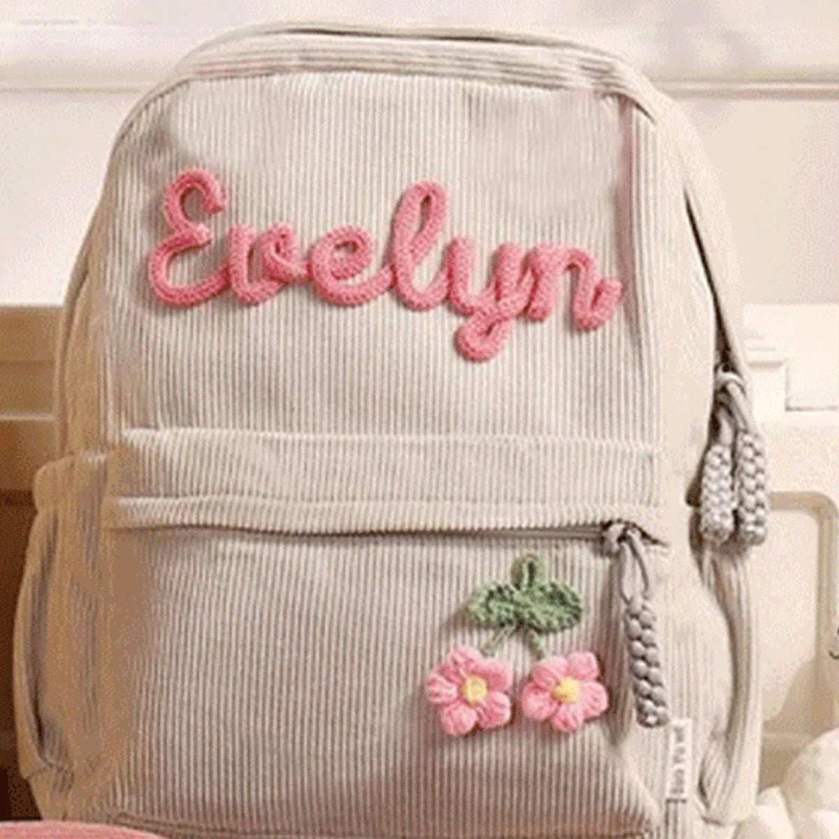 Helles beige Samtfell-Rucksack mit dem Namen Evelyn in rosa Garn und kleinen Blumenverzierung