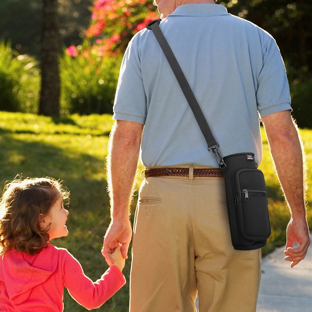 A man is carrying a black sling water bottle carrier bag while holding the hand of a young girl outdoors.