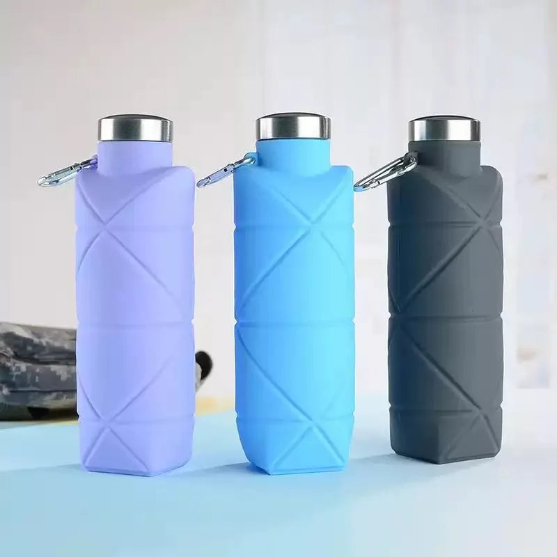Three collapsible silicone travel water bottles in purple, blue, and gray standing upright on a light surface.