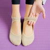 A pair of beige breathable women's Pilates and yoga socks being held by a hand against a purple background.