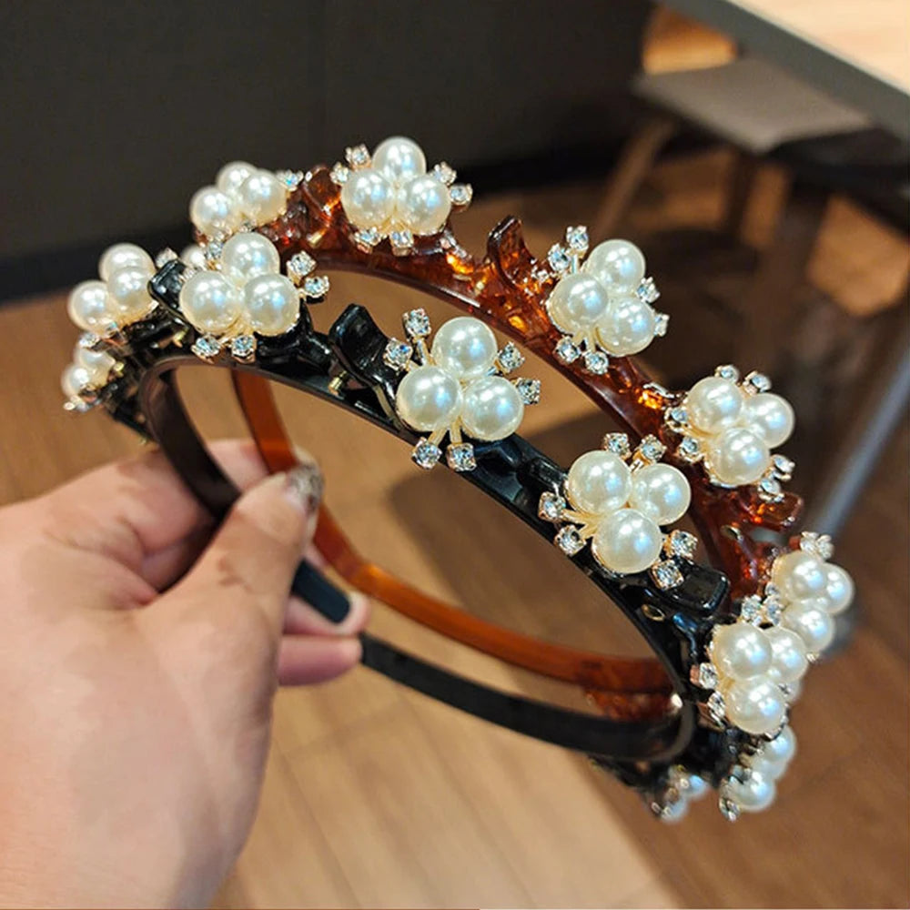 A hand holds a double layer headband featuring white pearls and clear rhinestones set in dark brown and black metalwork.