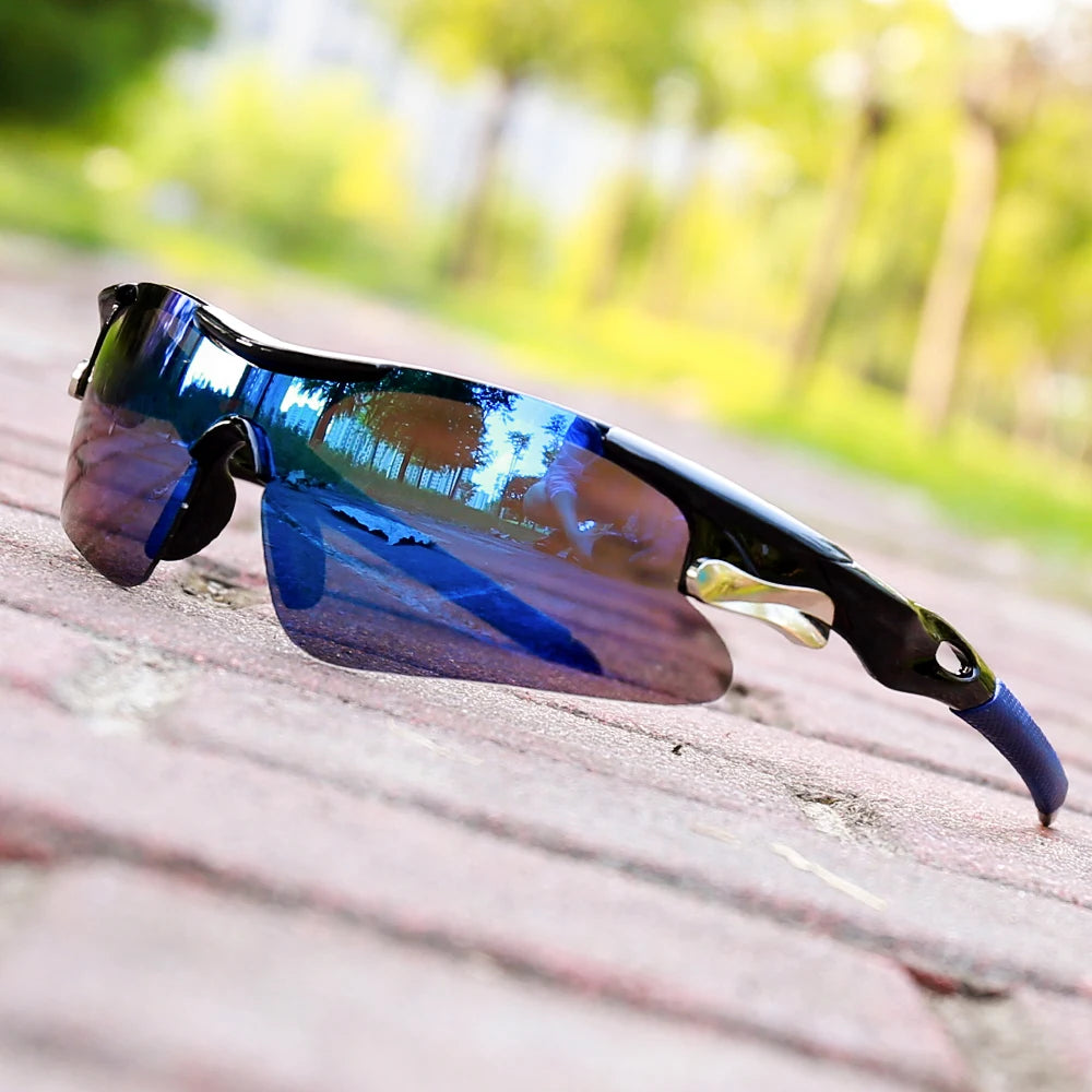 A pair of blue and purple sport sunglasses resting on a wooden surface with a blurred green outdoor background.