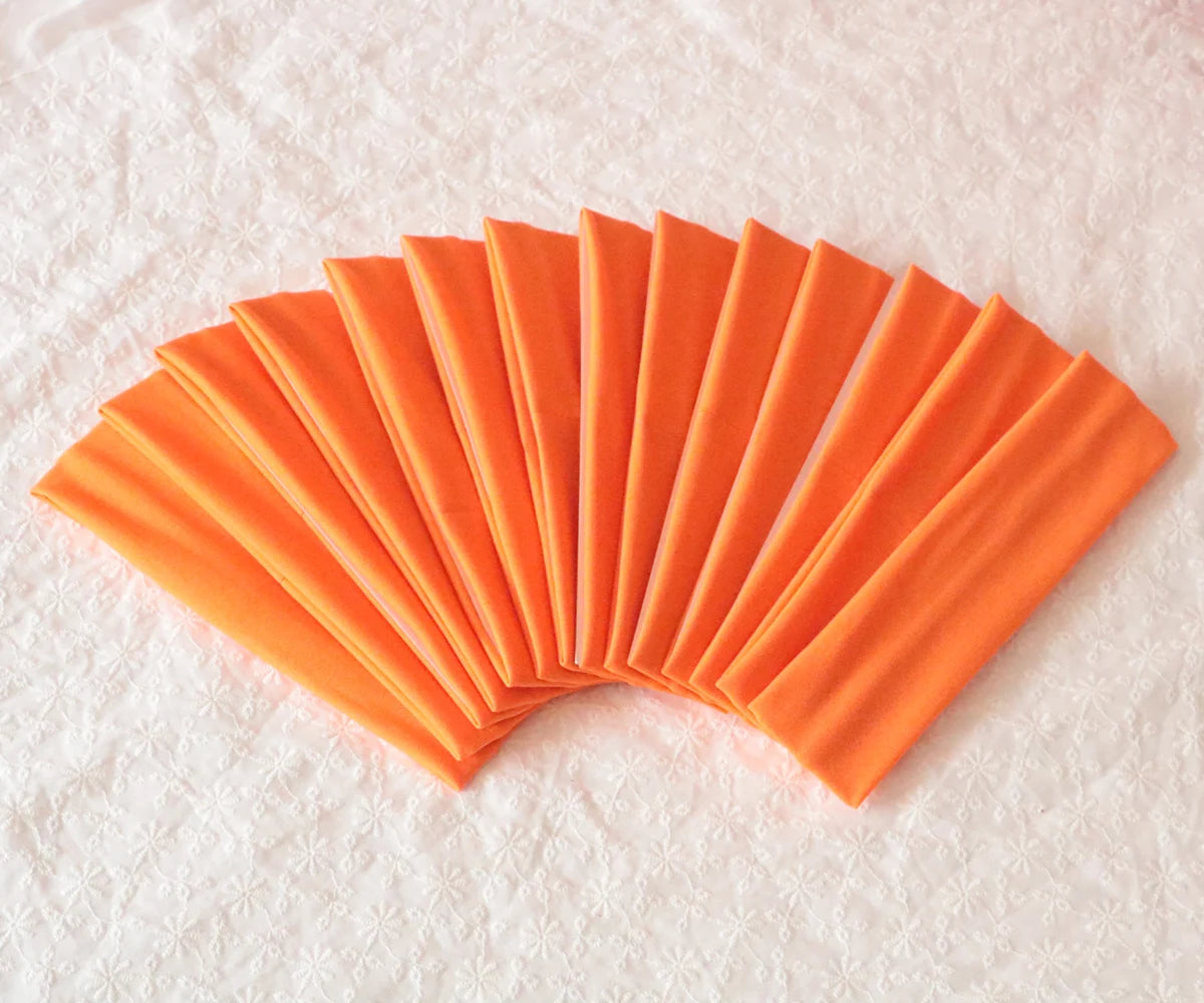 A fan of bright orange elastic headbands arranged in a semi-circle on a white surface.