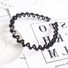 A black, wavy double layer pearl and rhinestone headband lying on a white surface next to paper.