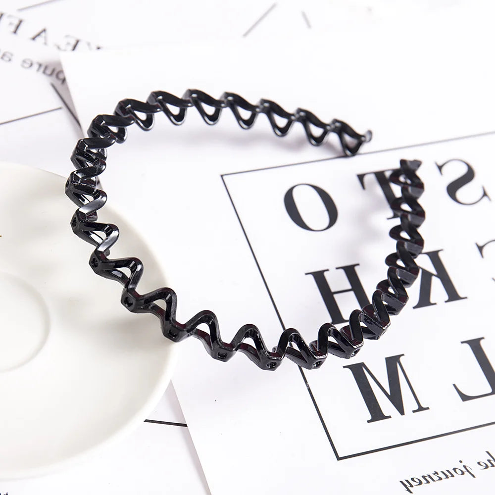 A black, wavy double layer pearl and rhinestone headband lying on a white surface next to paper.