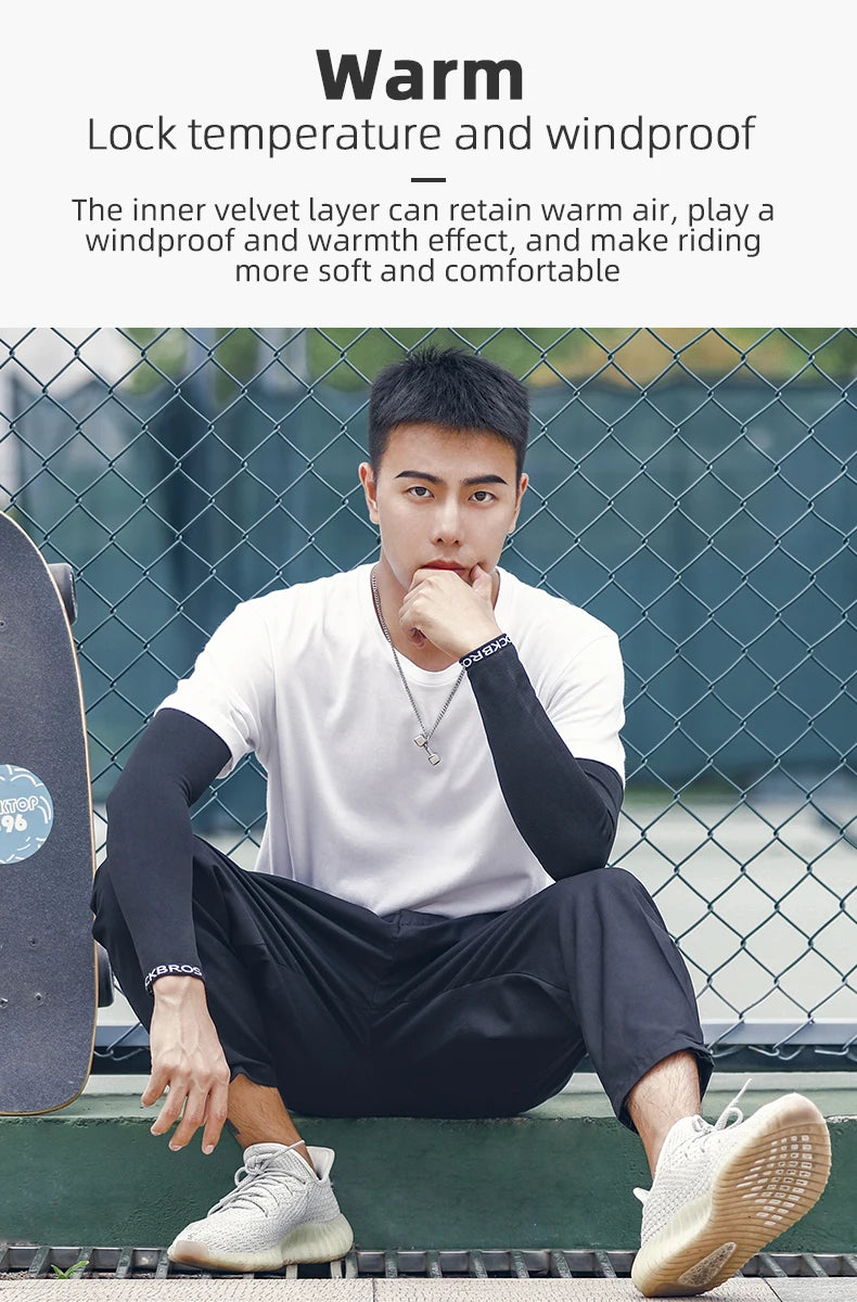 A young man wearing black cycling arm sleeves and a white shirt sits outdoors against a chain-link fence.