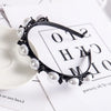 Black headband adorned with white pearls and rhinestones resting on white paper.