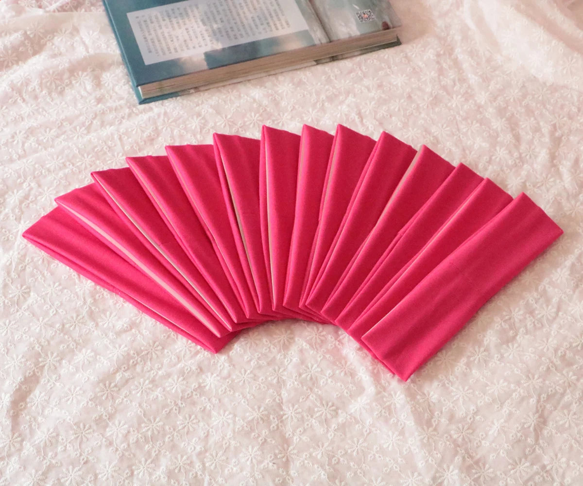 A fan of bright pink elastic headbands arranged in a semi-circle on a white fabric.