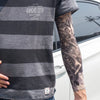 A person wearing a gray striped t-shirt displays a full sleeve tattoo on their arm.