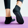 A close-up of black breathable women's yoga socks with small dots on the sole resting on a purple mat.