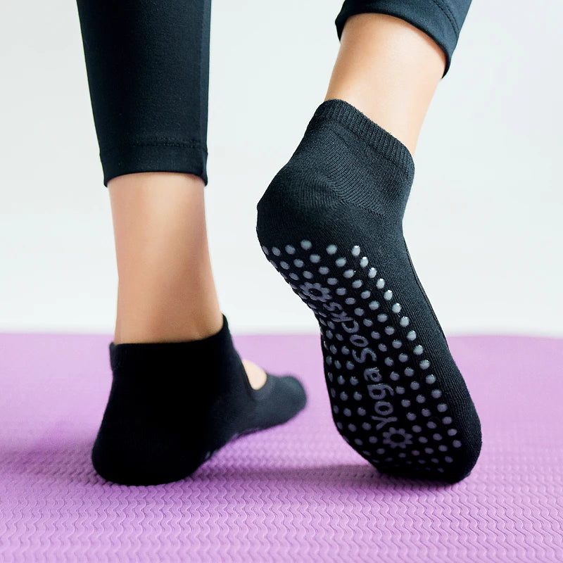 A close-up of black breathable women's yoga socks with small dots on the sole resting on a purple mat.