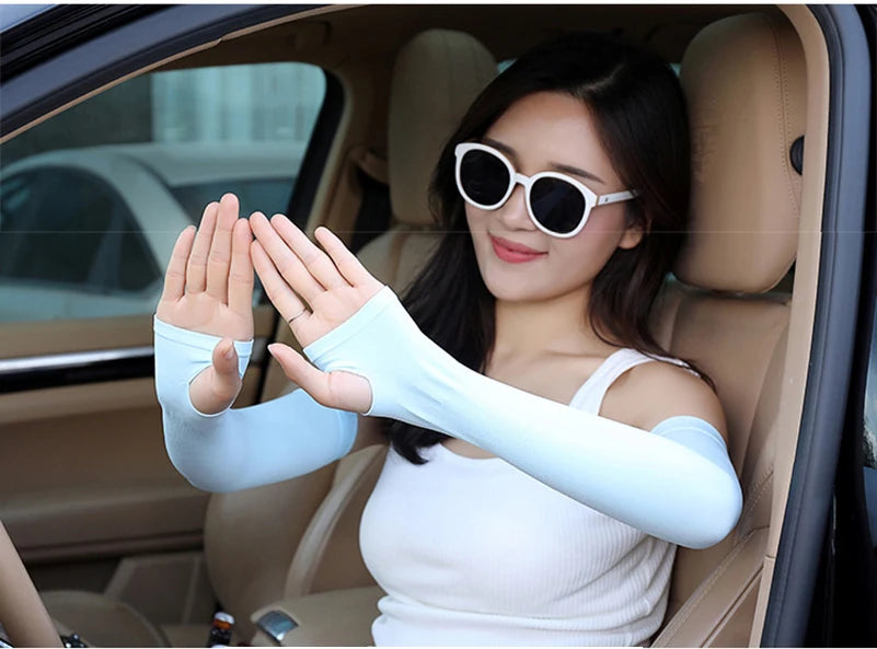 A woman wearing white fingerless arm sleeves and sunglasses is seated in a car interior.