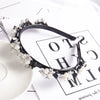 A black headband adorned with white pearls and rhinestones, displayed on a white background.