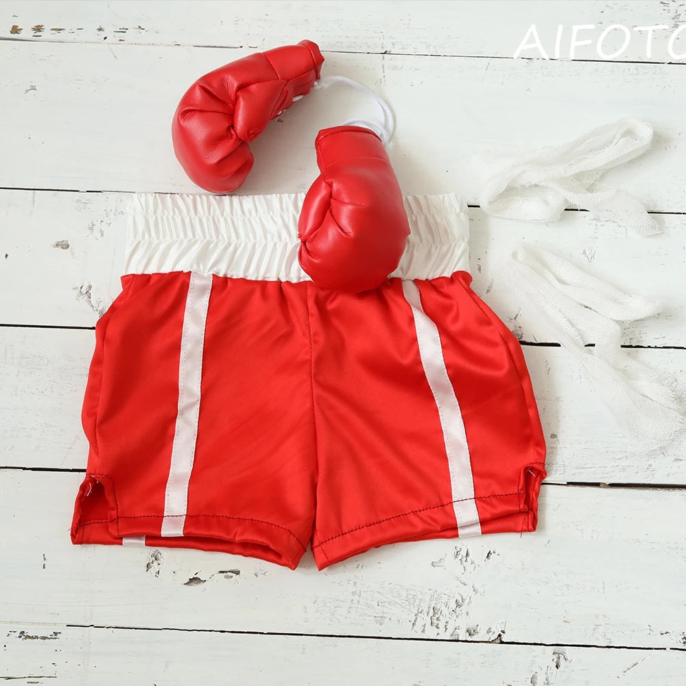 Guantes de boxeo rojos y pantalones cortos rojos con rayas blancas, exhibidos sobre una superficie de madera blanca.