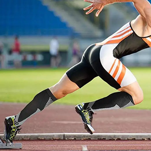 Una persona con medias de compresión negras realizando un estiramiento o ejercicio dinámico en una pista de atletismo.