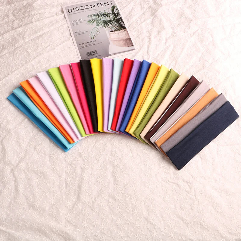 A collection of multi-use elastic headbands in various colors and shades laid out on a light fabric.