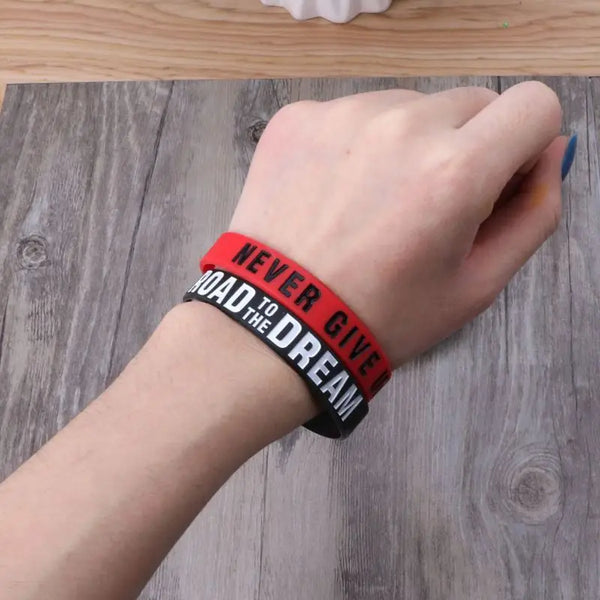 A hand wearing a red silicone elastic bracelet with the text NEVER GIVE UP THE DREAM on it.