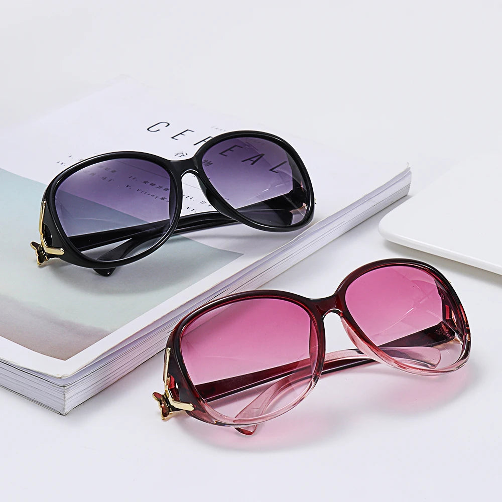 A pair of vintage oversized retro sunglasses in a pinkish-red tint resting on a white surface next to a book.