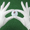 A pair of white golf gloves holding a white golf ball with the number 1 on it against a green background.