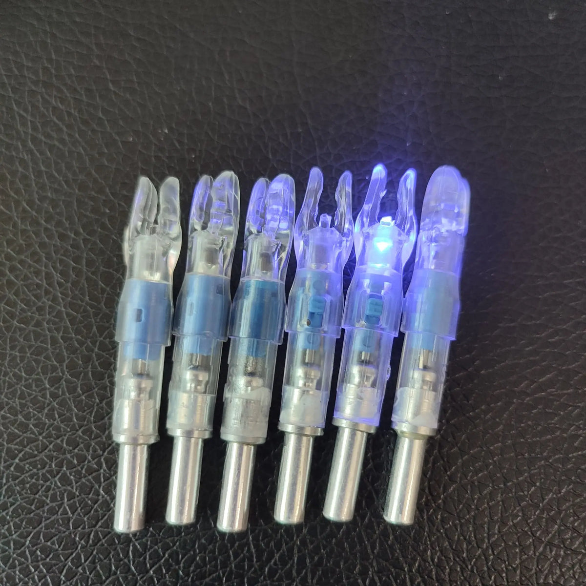 A row of lighted arrow nocks for archery, showing various plastic and metal components.