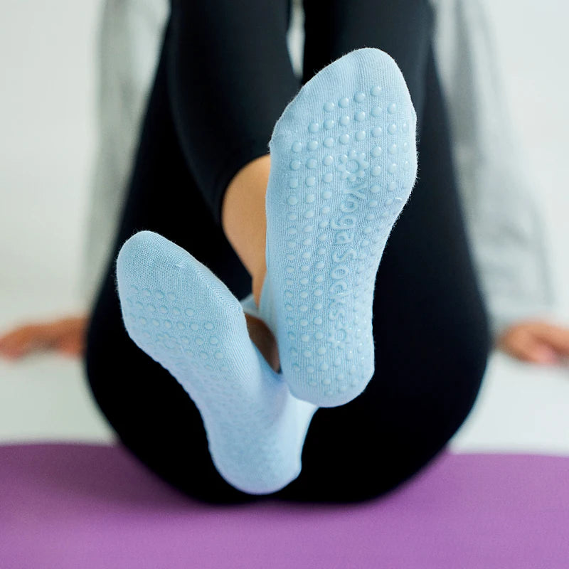 A person wearing light blue textured yoga socks is shown on a purple mat.