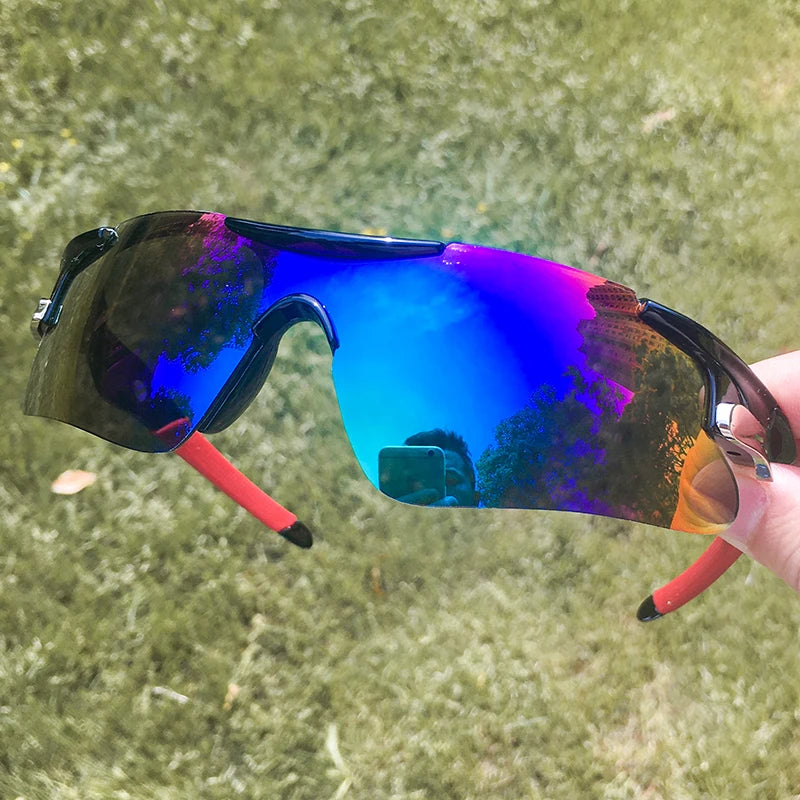A pair of blue polarized sport sunglasses with purple and orange reflections resting on a hand against a green outdoor backgr