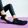 A pair of black breathable women's Pilates and yoga socks worn on a purple mat.