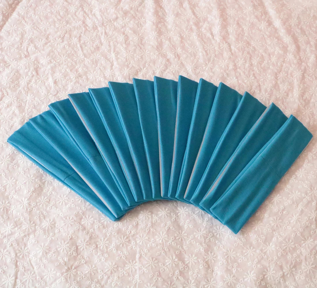 A fan of teal elastic headbands arranged in a semi-circle on a pink textured surface.