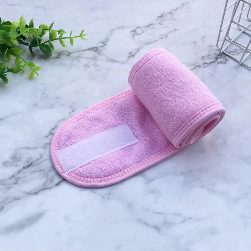 A pink, absorbent facial or spa towel with a white strip is rolled and displayed on a marble surface.
