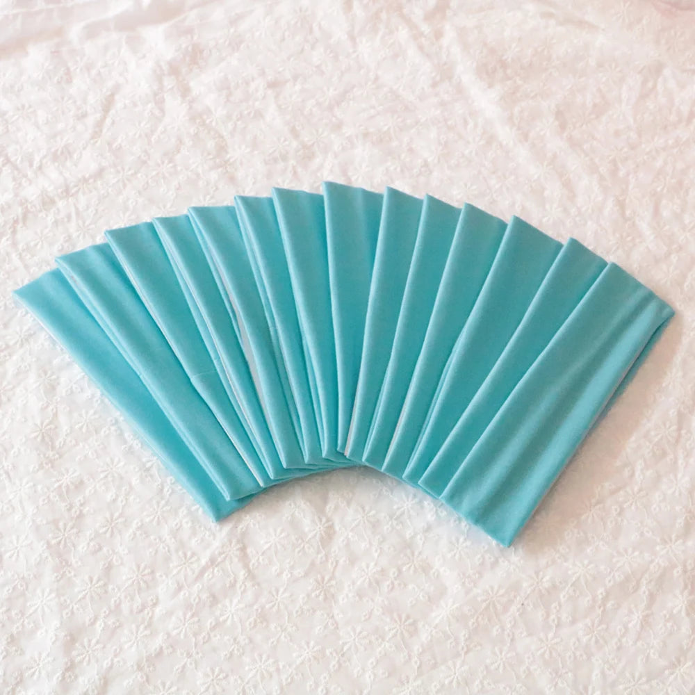 A fan of teal elastic headbands folded and displayed on a white textured surface.