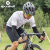 A male cyclist wearing a white shirt and black cycling gear riding a bicycle outdoors.
