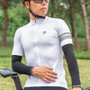 A person wearing a white cycling jersey and black arm sleeves is riding a bicycle outdoors.