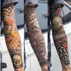 A close-up of a person wearing various reusable UV protection tattoo arm sleeves featuring detailed black and colored designs