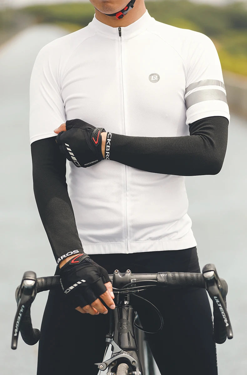 A man wearing a white cycling jersey and black arm sleeves is holding a bicycle handlebar.
