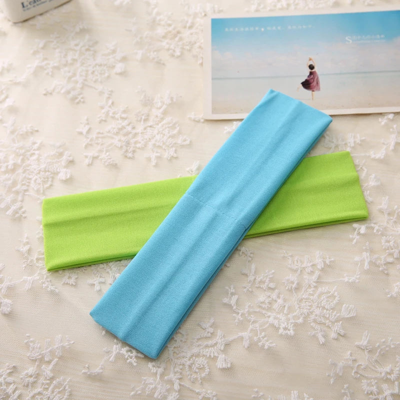 A light blue elastic headband is displayed next to a lime green one on a white lace surface.
