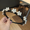 A close-up of a black headband decorated with white pearls and clear rhinestones being held by a hand.