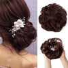 A close-up of dark brown messy curly hair bun extensions styled with white flowers and delicate beads.