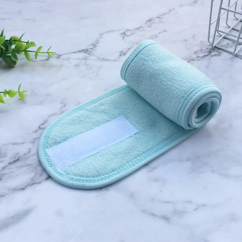 A light mint green absorbent facial or spa towel rolled up and placed on a white marble surface.