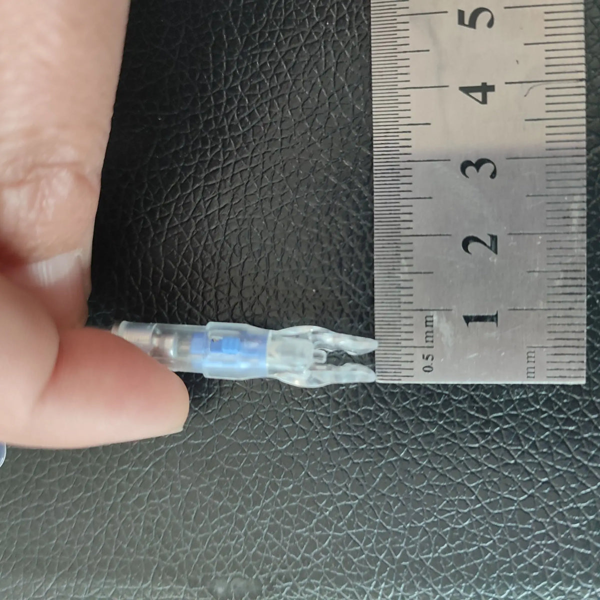 A clear plastic lighted arrow nock is shown next to a ruler for scale.